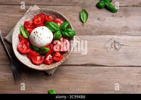 Tomatensalat mit Burrata und Basilikum auf rustikalem Holztisch, Blick von oben, Kopierraum. Gesunder hausgemachter Salat mit Burrata-Ball, Vorlage. Stockfoto