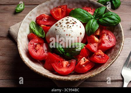 Tomatensalat mit Stracciatella-Weichkäse und Basilikum in Nahaufnahme. Gesunder hausgemachter Salat mit Burrata-Ball. Stockfoto
