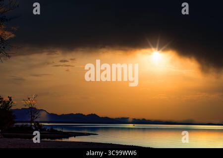 Beeindruckender Blick über den Chiemsee mit Blick auf die Alpen bei Sonnenuntergang und sich nähernden Wolken und Reflexionen auf dem Wasser Stockfoto