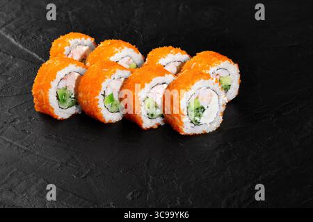 Kalifornische Uamaki-Sushi-Brötchen bedeckt mit orangenem tobiko fliegendem Fischrogen auf schwarzem Schiefergrund Stockfoto