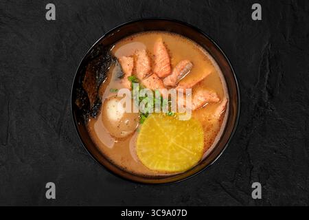Lachsmiso-Suppe mit Ei, eingelegtem Rettich, Algen und grünen Zwiebeln in einer Schüssel auf dunklem Hintergrund Stockfoto