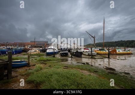 Vertäute Boote unter einem stürmischen Himmel. Blick auf den Kai bei Ebbe am Fluss Deben in der historischen Stadt Woodbridge in Suffolk, Großbritannien. Stockfoto