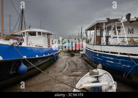 Boote sitzen auf Schlamm unter stürmischem Himmel. Blick auf den Kai bei Ebbe am Fluss Deben in der historischen Stadt Woodbridge in Suffolk, Großbritannien. Stockfoto