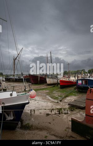 Woodbridge, Suffolk, Großbritannien: Boote sitzen auf Schlamm unter stürmischem Himmel. Blick auf den Kai bei Ebbe auf dem Fluss Deben in der historischen Stadt Woodbridge. Stockfoto