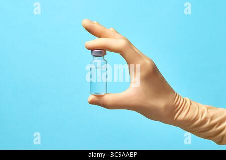 Hand in Handschuhen hält eine transparente Flasche mit einem Impfstoff auf blauem Hintergrund. Die Affenpockenschutzimpfung. Modellerstellung und Kopierbereich Stockfoto