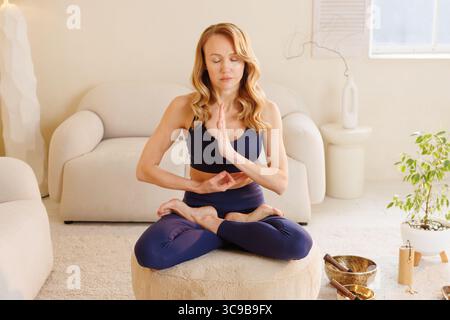 Junge Frau übt Achtsamkeitsmeditation in Lotusposition für einen gesunden Lebensstil und innere Balance zu Hause Stockfoto
