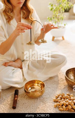 Weibliche Hände mit Tingsha-Becken, die ein Meditationsritual für Achtsamkeit, spirituelle Heilung und Entspannung zu Hause durchführen Stockfoto