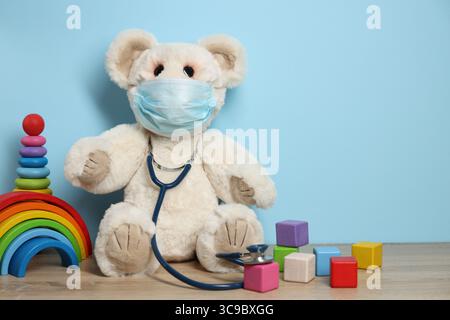 Kinderärztliches Konzept. Spielzeug, medizinische Maske und Stethoskop auf Holztisch vor hellblauem Hintergrund, Platz für Text Stockfoto