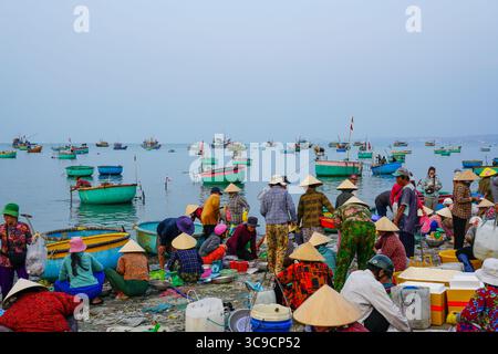 Mui ne, Vietnam, 22. März 2025: Geschäftiger Fischmarkt am Meer mit Fischern in traditioneller Kleidung Stockfoto