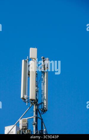 Eine Nahaufnahme eines modernen Telekommunikationsturms mit weißen Antennen und Kabeln, der hoch vor einem wolkenlosen blauen Himmel steht. Stockfoto