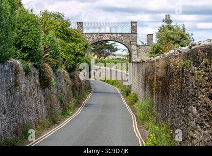 Enge Landstraße mit Steinmauern, die durch einen rustikalen Bogengang unter einem bewölkten Himmel in einer ländlichen Umgebung von South Sands Devon UK führt Stockfoto