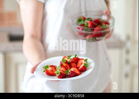 Nahaufnahme von weiblichen Händen, die zwei Teller mit geschnittenen ​​and ganzen Erdbeeren halten, gesunde Snacks zubereiten Stockfoto