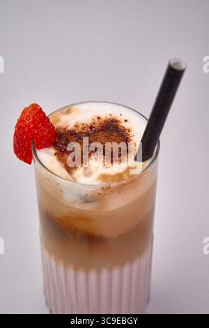Cremiges Erdbeergetränk mit Frosteis und Schlagsahne in einem großen Glas mit gestreiftem Strohhalm, garniert mit einer frischen roten Beere. Stockfoto