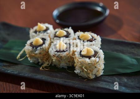 Köstliche Sushi Rolls serviert auf einem Schieferteller mit Sojasauce zum Dippen, mit cremigen Toppings und frischen Zutaten für ein authentisches Erlebnis Stockfoto