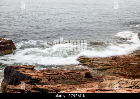 Wellen krachen bei Sonnenaufgang sanft gegen die zerklüfteten Felsen entlang der Küste und schaffen eine ruhige Atmosphäre. Das sanfte Licht reflektiert das Wasser und verbessert so die Qualität Stockfoto