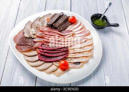 Fleischplatte mit köstlichen Stücken Schinken, Kirschtomaten und Fleisch mit Sauce auf weißem Holzhintergrund. Stockfoto