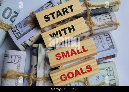 Das Wort beginnt mit kleinen Toren auf gestapelten Holzwürfeln mit Dollarwährung auf dem Tisch. Geschäfts- und Finanzkonzept Stockfoto