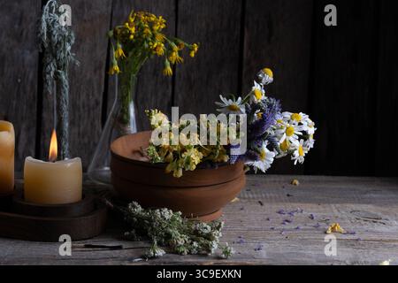 Strauß von wilden Kräutern in Holzschale und Kerzen auf Holztisch Stockfoto