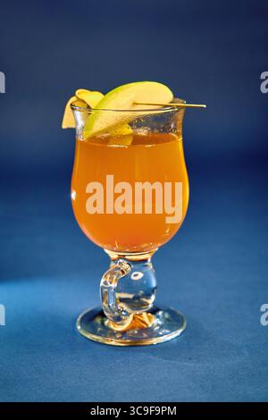 Ein erfrischendes Glas Orangengetränk garniert mit frischen Apfelscheiben vor einem glatten blauen Hintergrund, ideal zum Durstlöschen an einem warmen Tag Stockfoto
