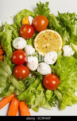 Leckerer Salat mit Kirschtomaten, Salatblättern, Zitrone, Gewürzen, Karotten und Wachteleiern auf weißer Platte. Draufsicht. Stockfoto
