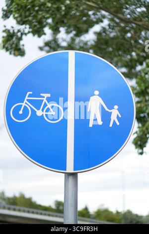 Blaues rundes Schild mit einem gemeinsamen Weg für Fahrräder und Fußgänger in einem grünen Stadtgebiet. Stockfoto