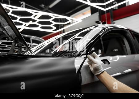 Vinyl-Verpackung Für Autos Mit Vollpaneel. Die großformatige Vinylfolie verwandelt das Außenmaterial des Fahrzeugs mit mattschwarzer Folie. Änderungen an der Anwendung der Autoverpackung Stockfoto