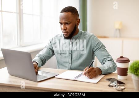 Schwarzer Geschäftsmann Arbeiten Notizen Und Mit Laptop Am Arbeitsplatz Stockfoto