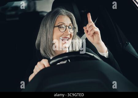 Reife Geschäftsfrau lächelt selbstbewusst, während sie an einem hellen Tag ein Auto fährt, und verkörpert Eleganz und Professionalität Stockfoto
