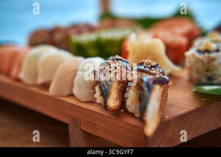 Eine atemberaubende Auswahl an frisch zubereiteten Sushi, die auf einer traditionellen Holzplatte präsentiert wird, mit einer Reihe von Farben und Texturen verschiedener Ing Stockfoto
