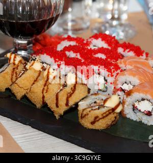 Eine Auswahl an Sushi-Brötchen, darunter gebratene, Lachs und Reh, serviert auf Schieferteller mit Rotwein auf festlichem Innentisch Stockfoto