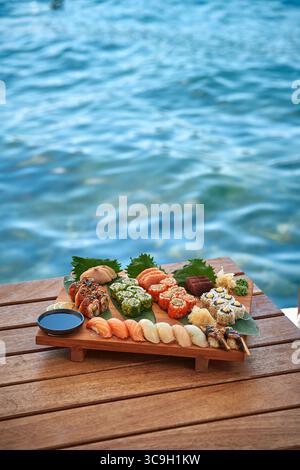 Eine bunte Auswahl an frischen Sushi und Sashimi serviert auf einem Holzteller mit malerischem Hintergrund, perfekt für ein kulinarisches Erlebnis im S Stockfoto