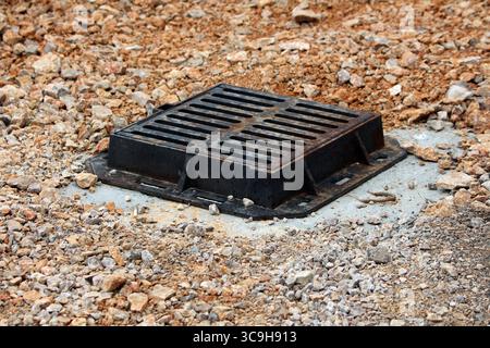 Ein stabiles schwarzes Metallgitter sitzt bündig in einem von Kies umgebenen Betonrahmen und sichert die Entwässerungsöffnung auf dem Boden Stockfoto