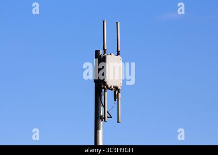 Eine kompakte Mobilantenne mit zwei vertikalen Sendern ist an einem Stahlmast montiert, der scharf vor einem wolkenlosen blauen Himmel umrissen ist und Draht symbolisiert Stockfoto