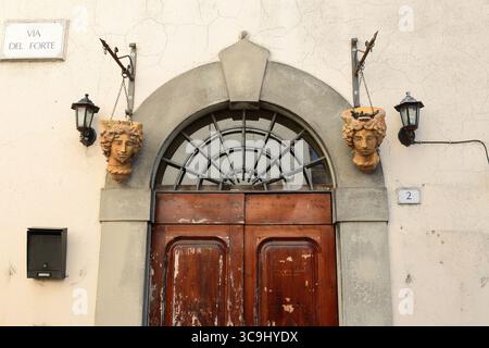 163 Wandlampen und hängende Pflanzgefäße auf beiden Seiten einer Holztür im Renaissancestil in der Via del Forte. Castiglione del Lago-Umbria-Italien Stockfoto