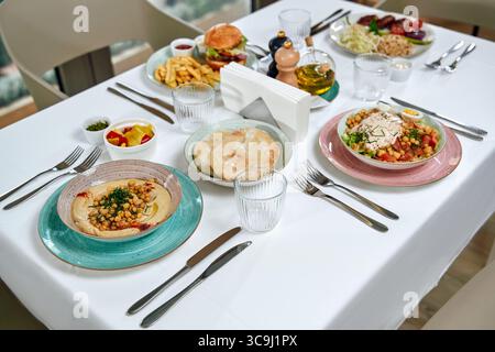 Ein wunderschön gestalteter Esstisch mit einer Auswahl an köstlichen Gerichten wie Salaten, Vorspeisen und Hauptgerichten in eleganter Umgebung. Stockfoto