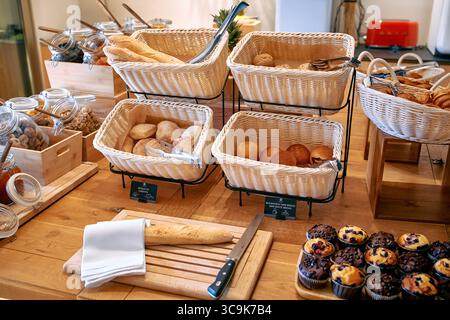Eine herrliche Auswahl an frisch gebackenen Waren einschließlich verschiedener Brotsorten, Gebäck und Desserts, die ordentlich auf einem Holztisch in einem einladenden s angeordnet sind Stockfoto