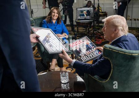 Präsident Donald J. Trump nimmt während seines Besuchs in Schottland 2025 an einem Interview im Fernsehen Teil. Trump wird gesehen, wie er gerahmte Titelseiten der Sun-Zeitung hält, während er gegenüber einer Gastgeberin sitzt, mit einer Produktionsperson und Kameraausrüstung im Hintergrund. Juli 2025. Bild mit freundlicher Genehmigung des Weißen Hauses. Stockfoto