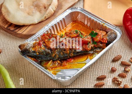 Köstlich zubereiteter gegrillter Fisch, garniert mit scharfer Tomatensauce und serviert mit frischen Zutaten, perfekt für ein köstliches Essen Stockfoto