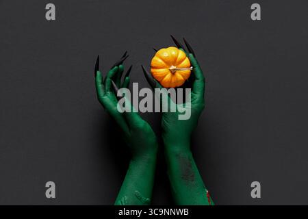 Grüne Hände der Hexe mit Kürbis auf schwarzem Hintergrund. Halloween-Feier Stockfoto