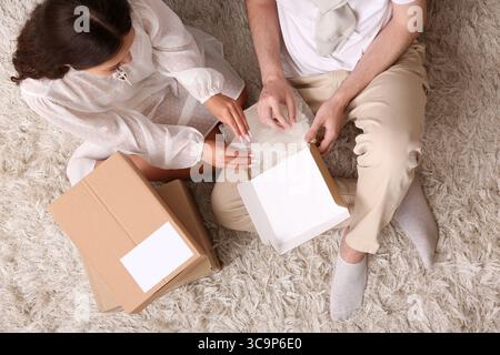 Junges Paar packt Paketkarton auf Teppich aus, Draufsicht Stockfoto