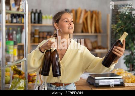 Die Käuferin untersucht Bierflaschen, wählt den richtigen Hersteller, nimmt verschiedene Flaschen aus dem Regal. Stockfoto