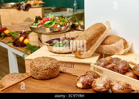Ein reichhaltiges Angebot an frisch gebackenem Brot und farbenfrohen Salaten, die elegant auf Holzplatten angeordnet sind, für ein besonderes kulinarisches Erlebnis Stockfoto