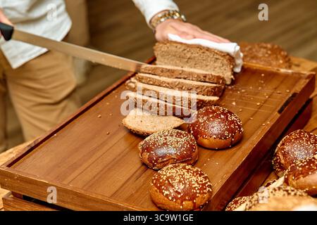 Handwerkliche Brotzubereitung: Ein kulinarisches Erlebnis mit frisch gebackenen Broten und Rolls, die zum Genuss geschnitten werden Stockfoto