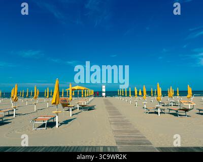 Liegestühle mit gelben Sonnenschirmen am Sandstrand. Geschlossene Sonnenschirme und leere Liegen bei windigem Wetter. Urlaubskonzept. Stockfoto