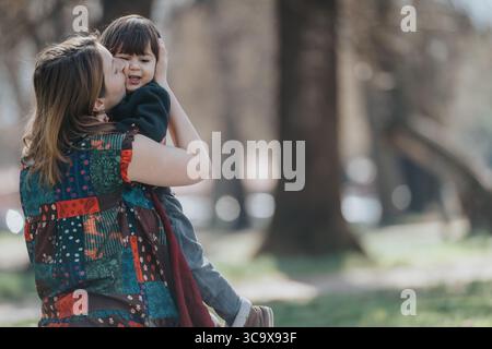 Mutter umarmt ihr lächelndes Kind liebevoll in einem ruhigen Park Stockfoto