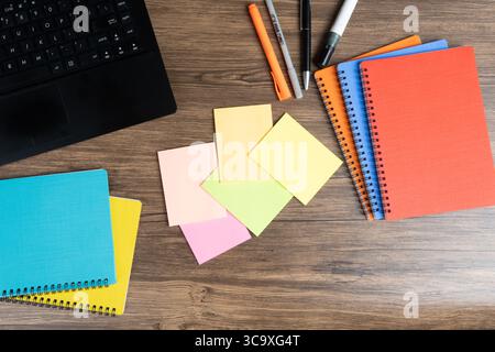 Draufsicht auf leere Haftnotizen auf einem Holztisch mit offenem Laptop, farbenfrohen Ordnern und Stiften. Stockfoto