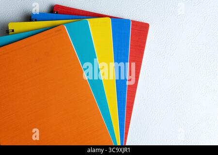 Nahaufnahme eines flachen Lay-Fotos von gestapelten bunten Spiralnotizbüchern auf weißem, strukturiertem Hintergrund. Ideal für Bildung, Büro, Schreibwaren und kreative Arbeiten Stockfoto