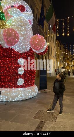 Weihnachten. Ein Kind bewundert eine große beleuchtete Weihnachtsmannfigur in festlicher Straßenlage. Die Nachtszene fängt die Magie und das Wunder von ein Stockfoto