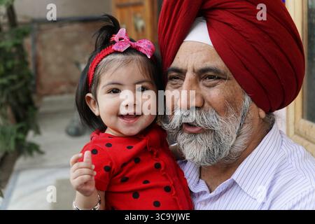Ein älterer Mann mit Turban umarmt ein lächelndes Kind, Rajasthan, Indien Stockfoto