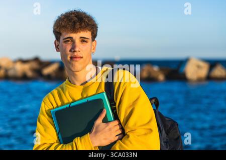 Junge Studentin, die Bücher am Meer bei Sonnenuntergang hält Stockfoto